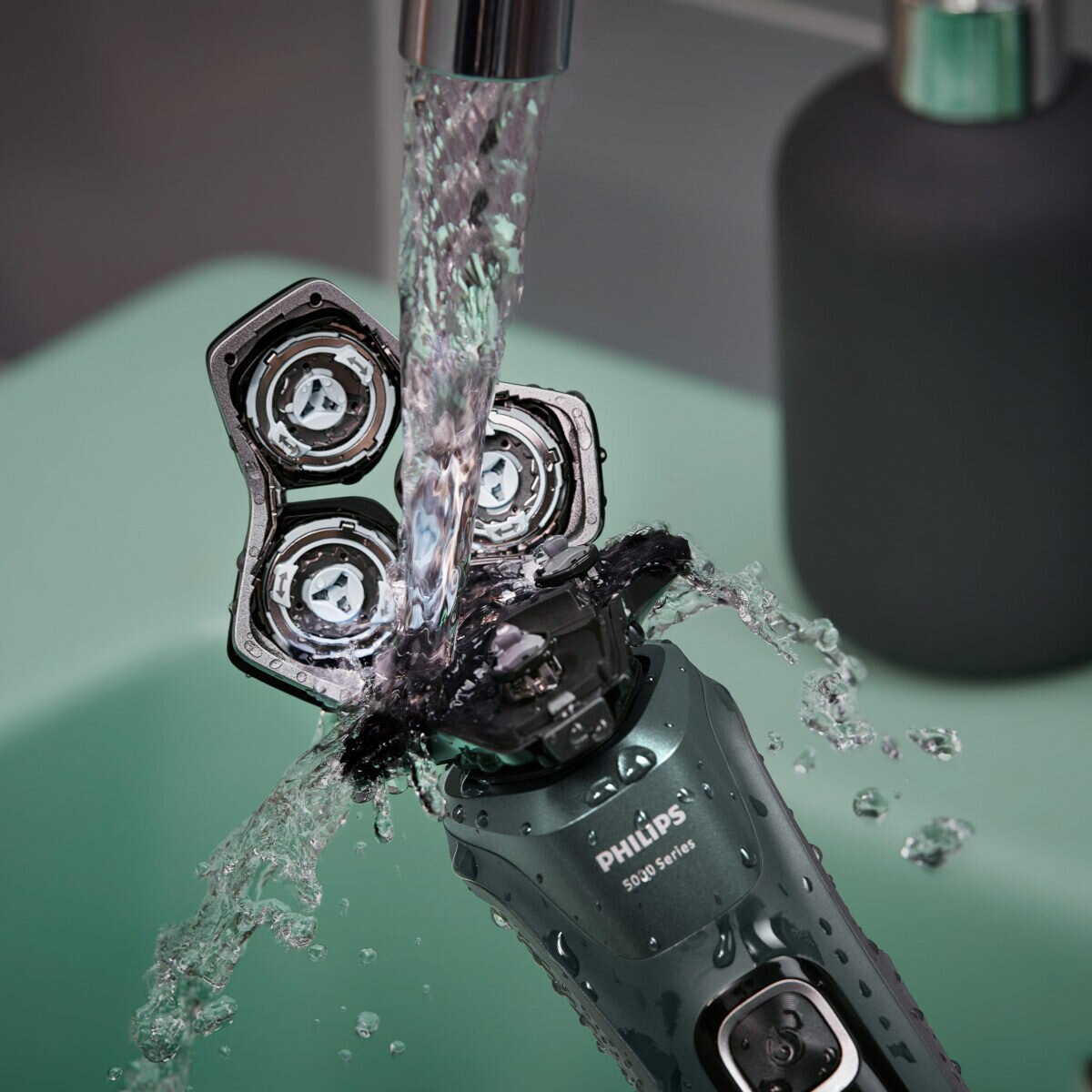Woda spływa po golarce Philips, z otwartą głowicą, nad zielonym zlewem.