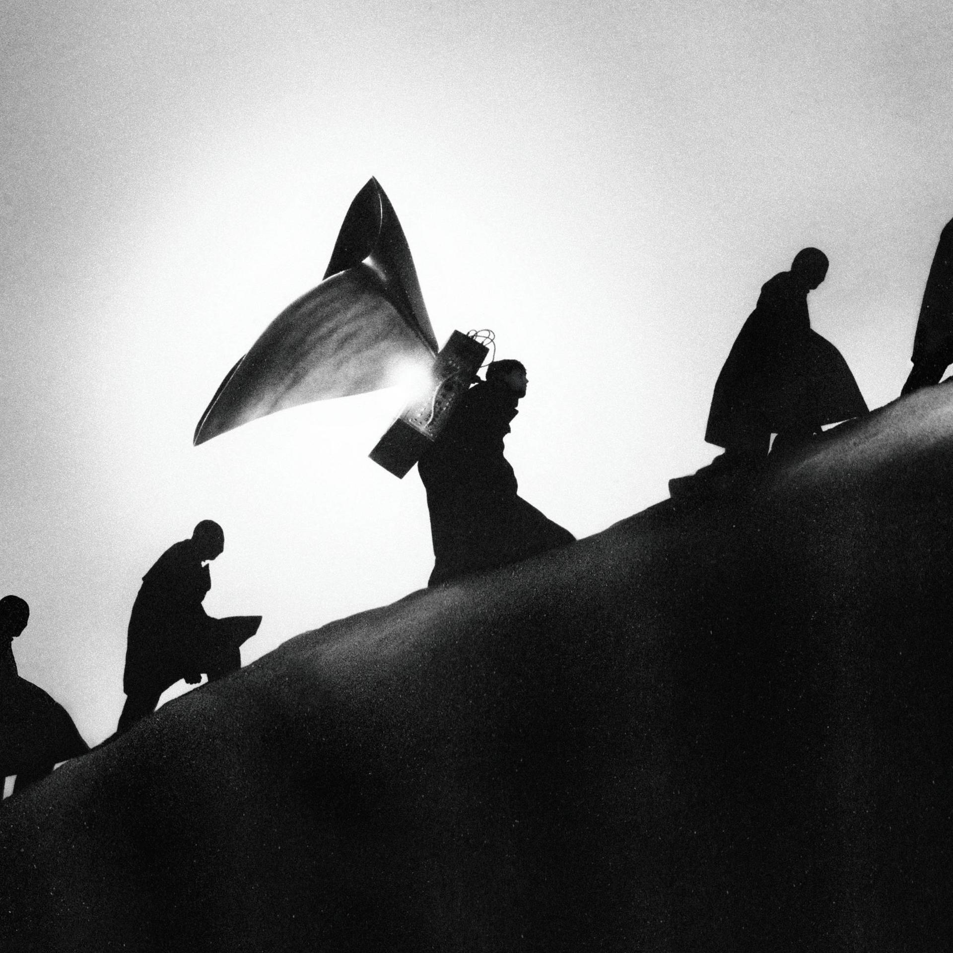 Schattenhafte Figuren, die ein Kreuz einen Hügel hinauftragen. Die Sonne ist hinter ihnen.