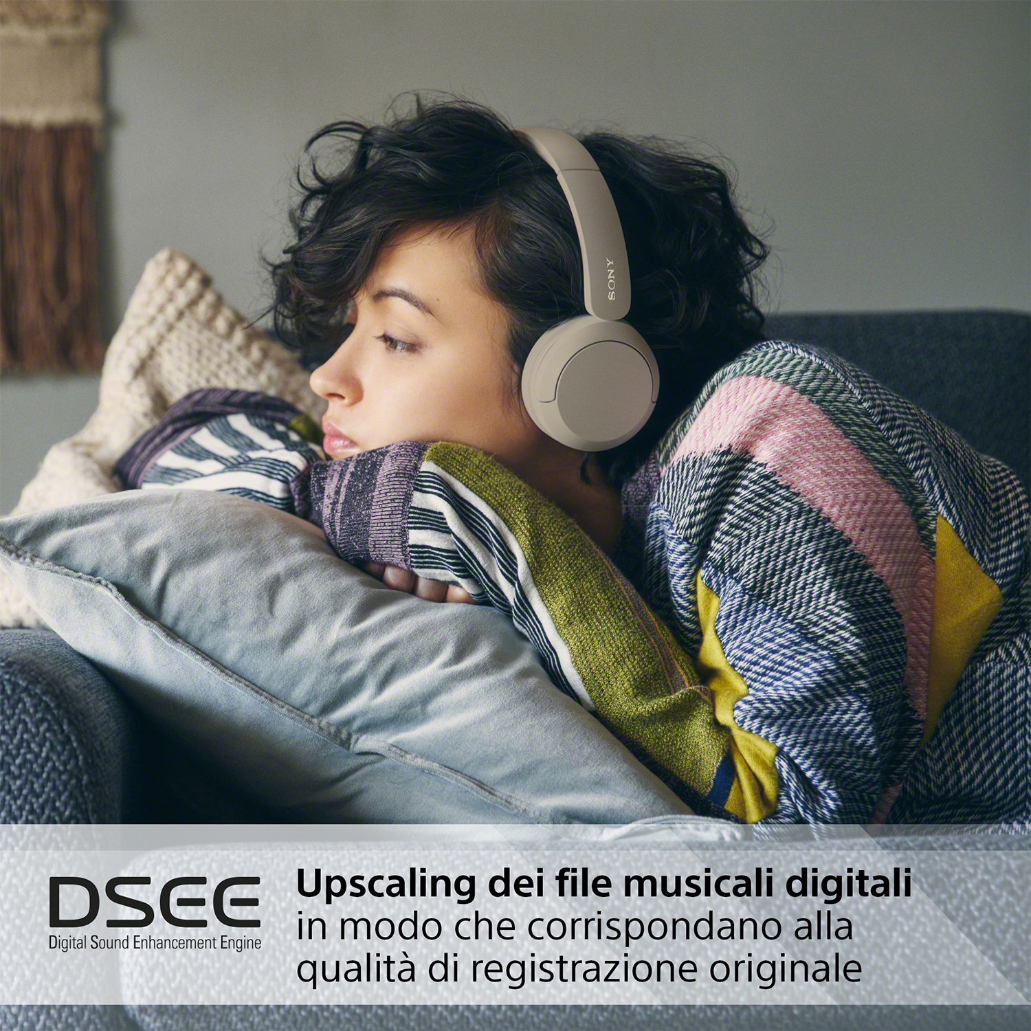 Una donna con cuffie grigie si riposa su un divano con una coperta. Testo in basso: DSEE, up-scaling musicale.