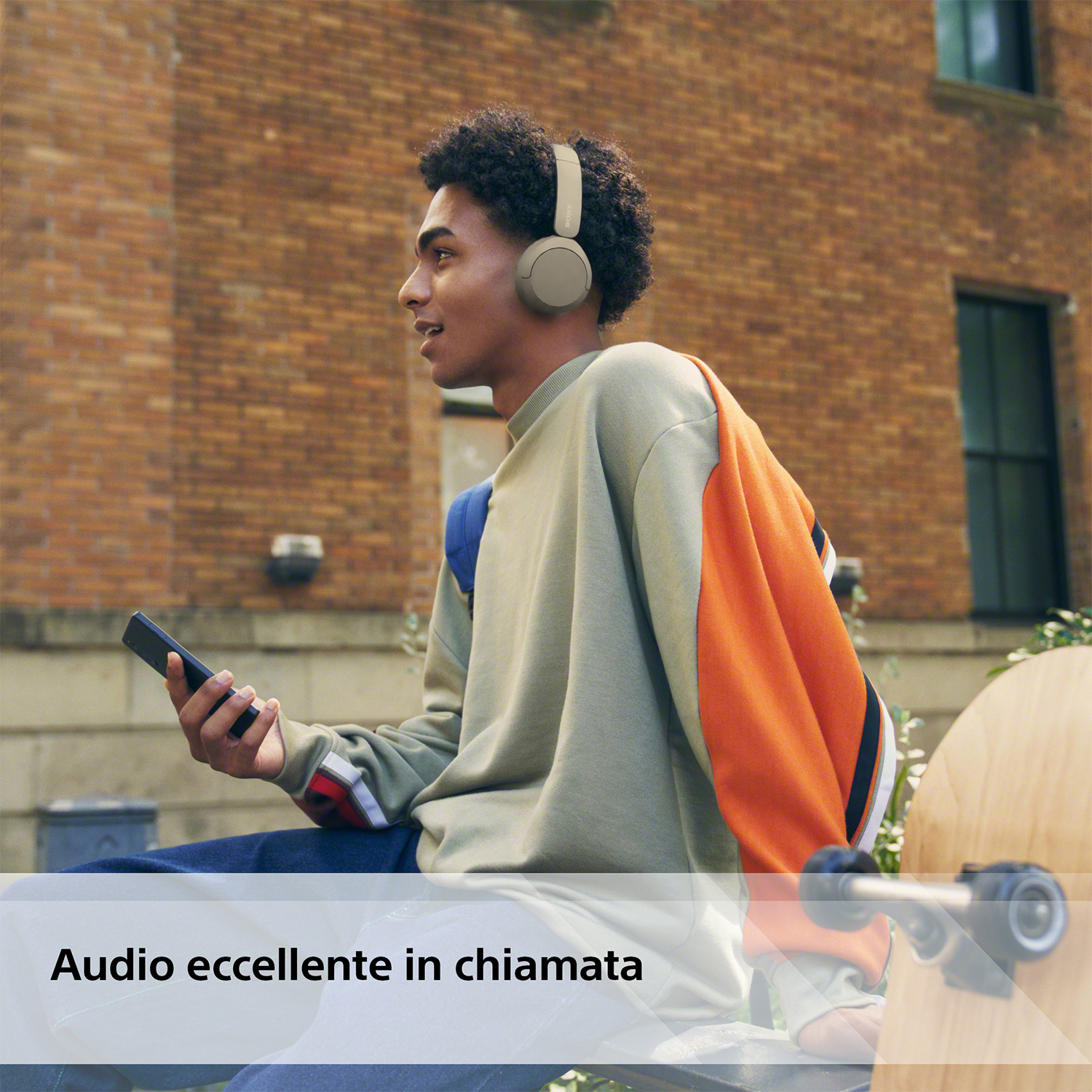 Un uomo con le cuffie ascolta musica. Tiene in mano un telefono e si trova all'aperto.