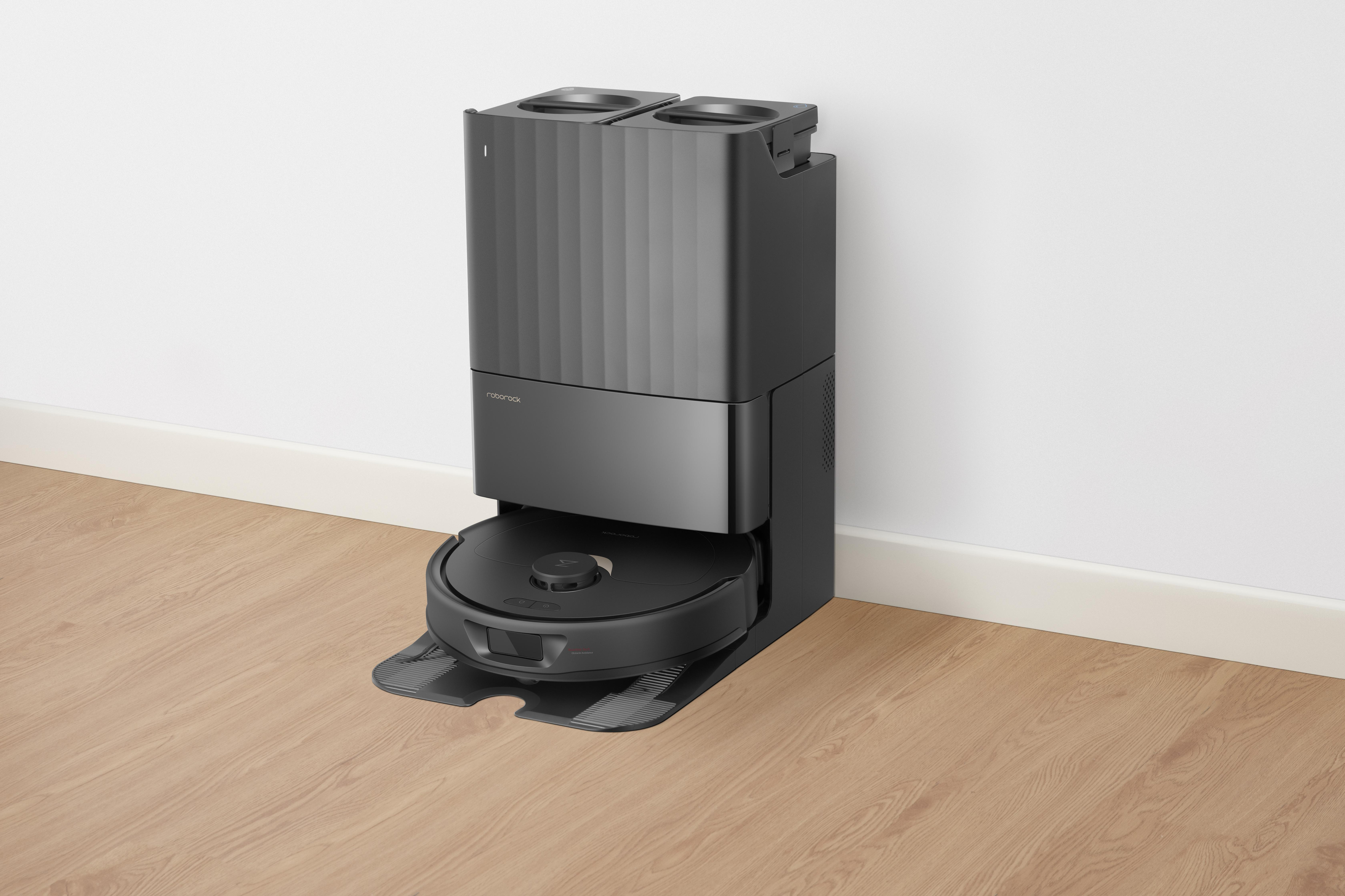 Schwarzer Roboter-Staubsauger und Ladestation auf einem Holzboden. Weißer Wandhintergrund.