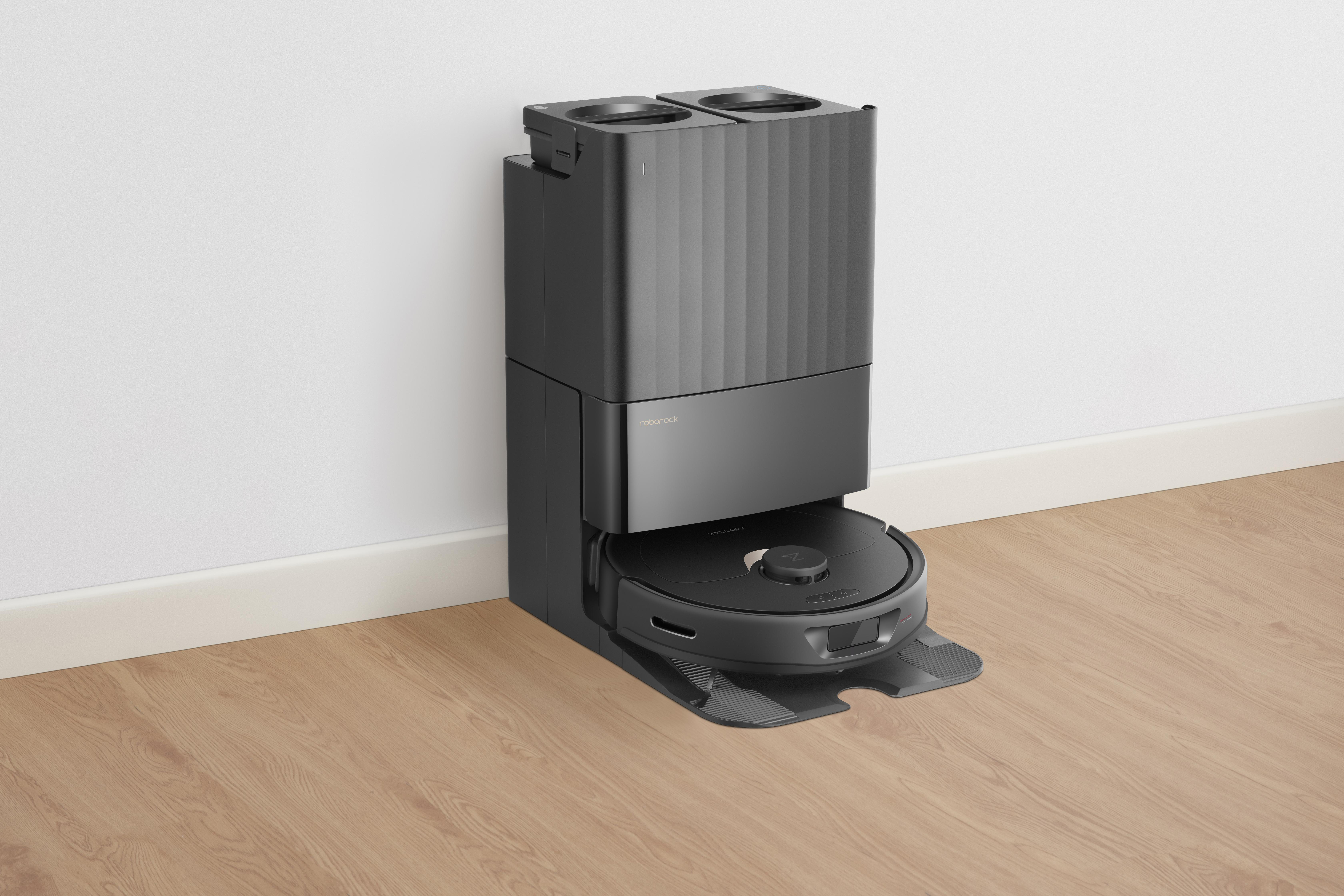 Ein schwarzer Roboter-Staubsauger mit Ladestation auf Holzboden vor weißer Wand.