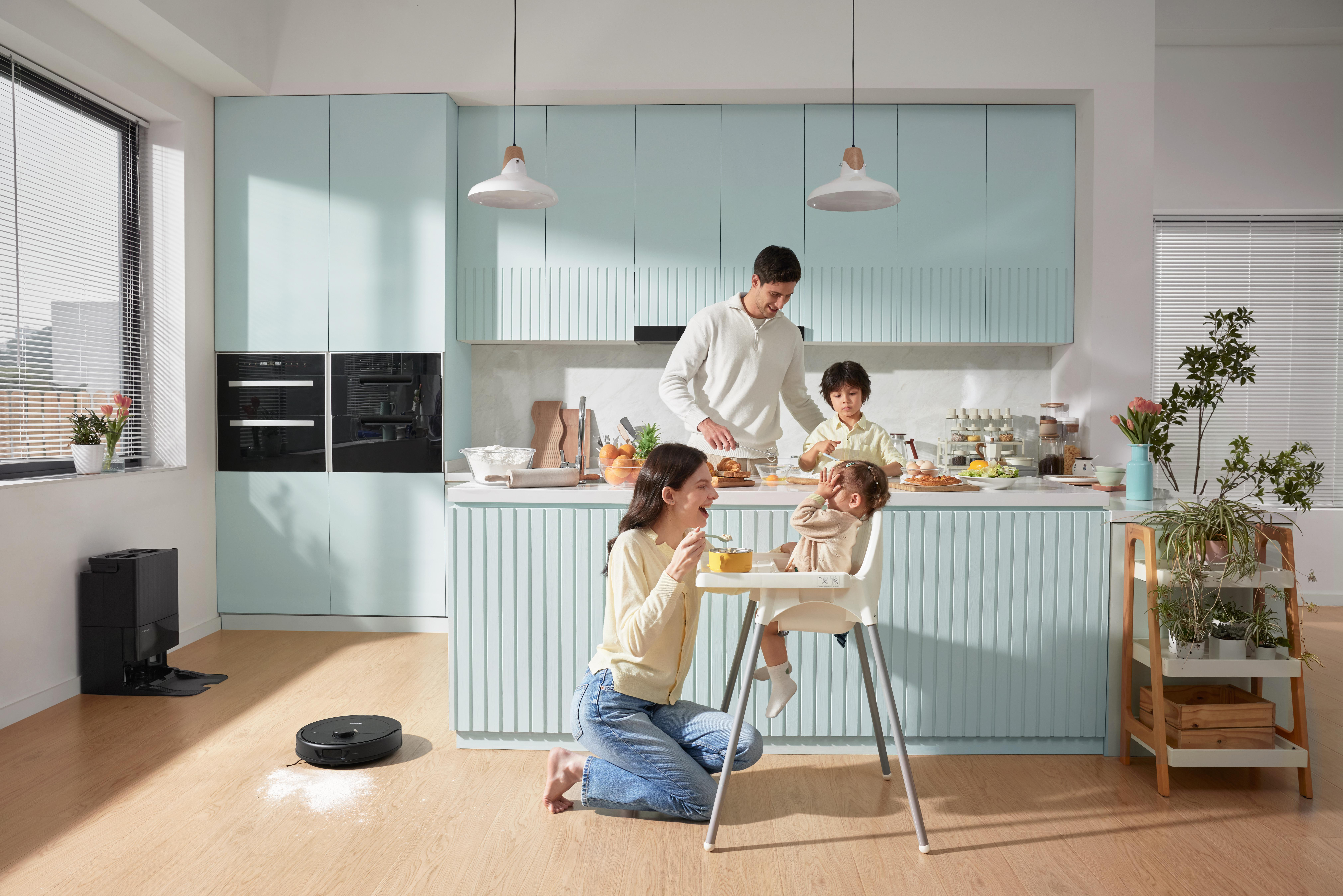 Eine Familie in einer modernen Küche. Eine Frau und ein Kind sitzen an einem Tisch, andere Familienmitglieder kochen.
