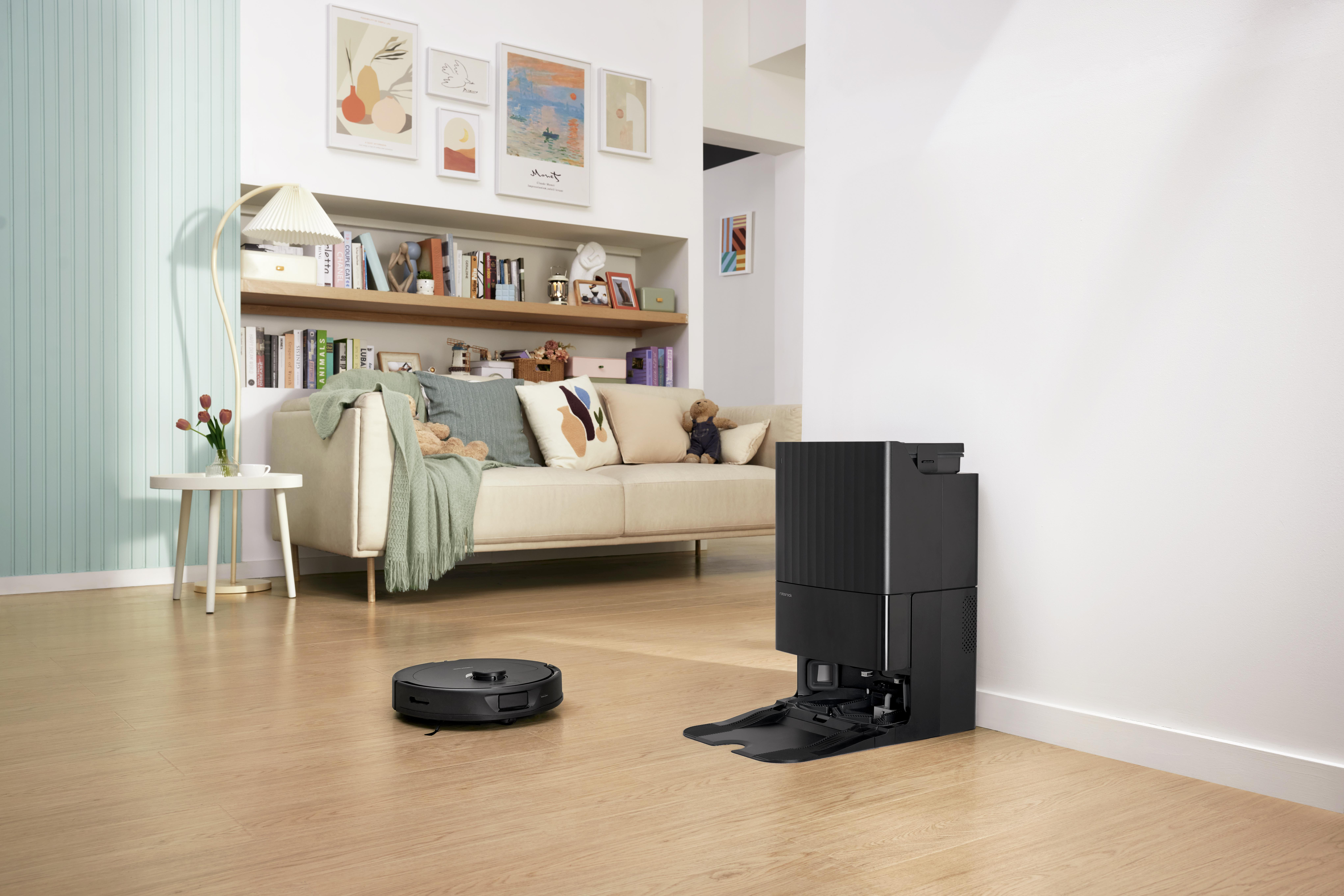 Ein Roboterstaubsauger und eine Ladestation in einem Wohnzimmer mit Sofa und Deko.