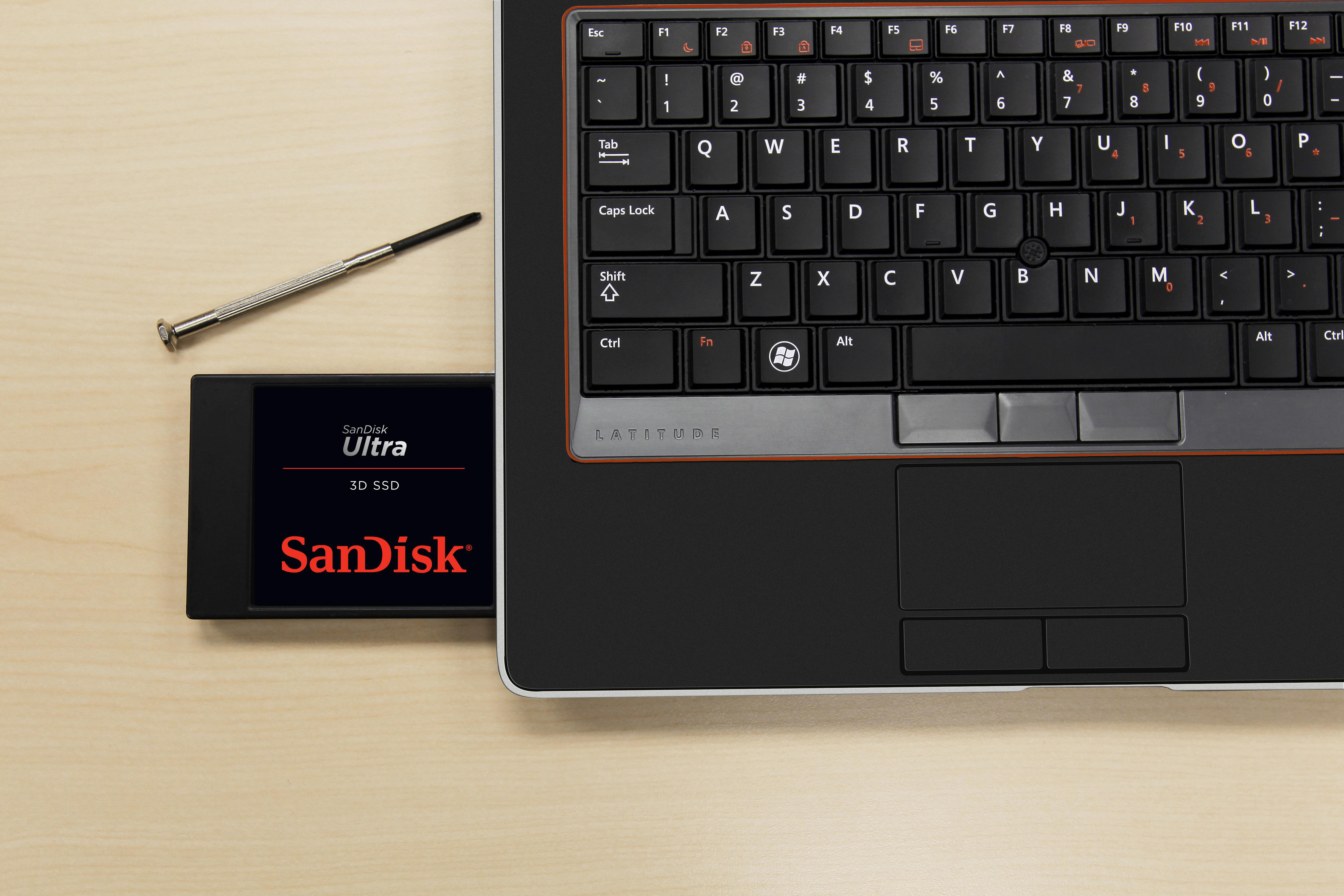 Ein Laptop, der mit einer Sandisk SSD daneben und einem Schraubendreher geöffnet ist.