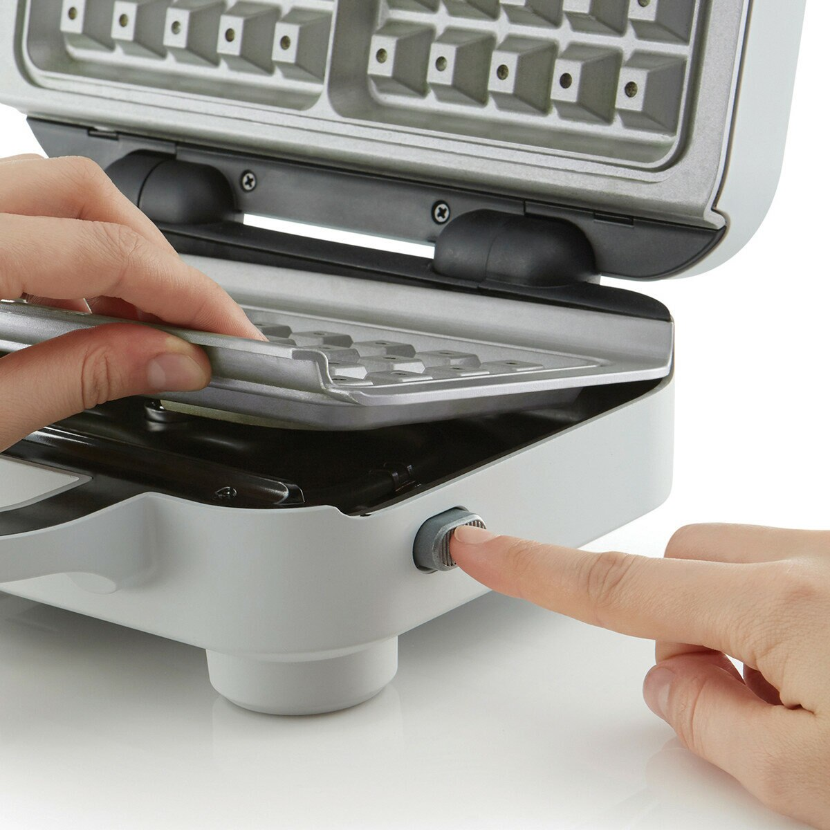 Osoba naciska przycisk na gofrownicy, aby ją otworzyć.