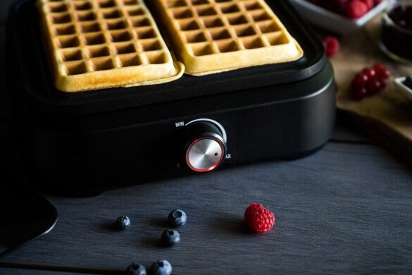 Gofrownica z dwoma goframi, otoczona borówkami i maliną.