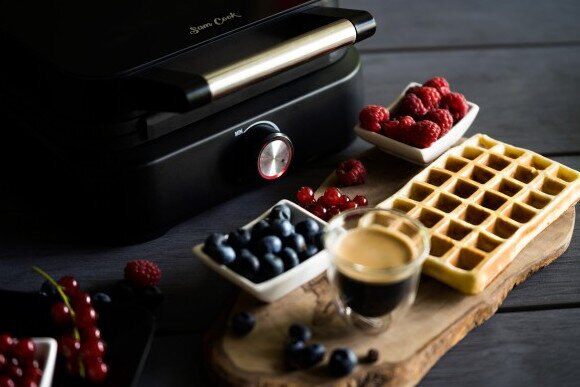 Gofrownica z goframi, borówkami, malinami i kawą na drewnianej desce.