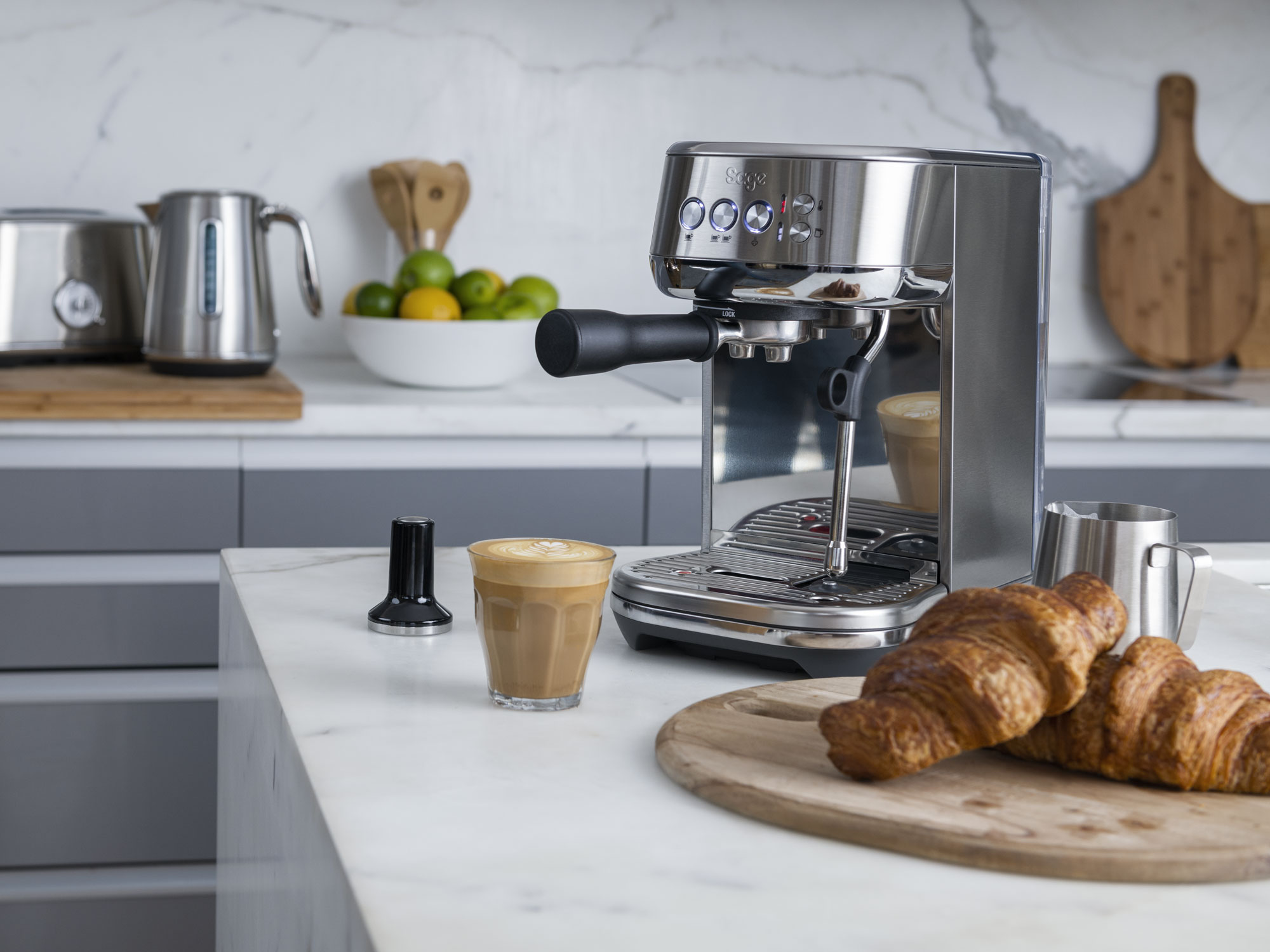Rozsdamentes acél eszpresszógép egy csésze lattéval és croissant-okkal márvány felületen.