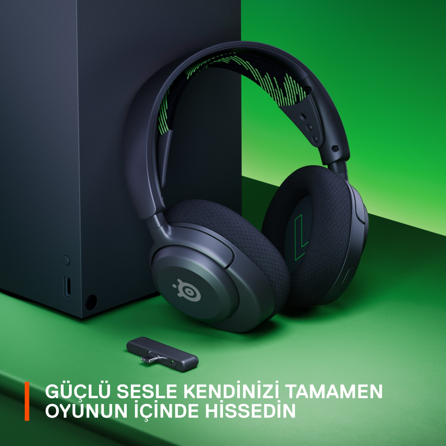 Siyah oyun kulaklığı ve alıcısı, siyah bir oyun konsolunun yanında. Yeşil ve siyah renk şeması.