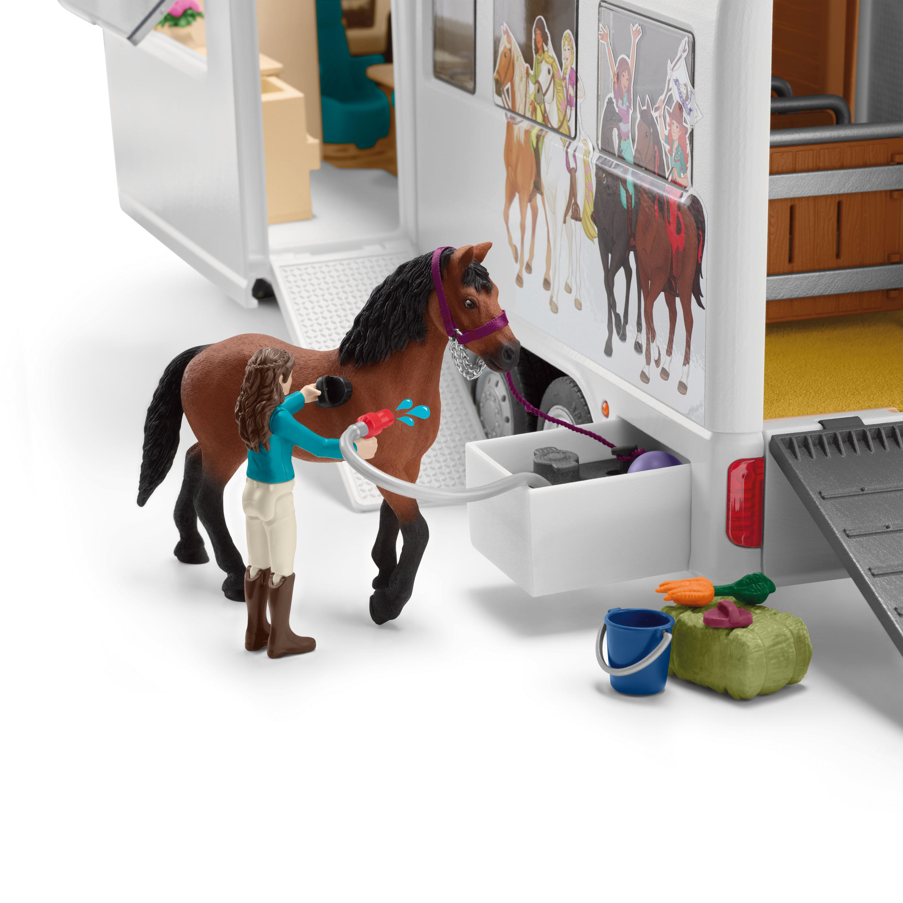 Eine Spielzeugszene, in der ein Pferd von einem Mädchen in der Nähe eines Anhängers gewaschen wird.