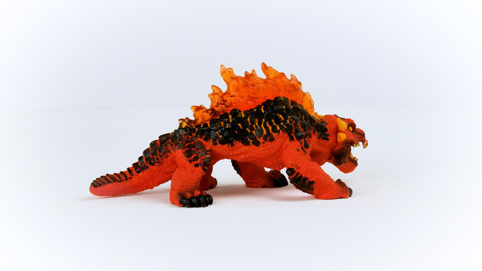Rotes und oranges Spielzeugmonster mit flammenartigem Kamm. Es steht auf einer weißen Oberfläche.