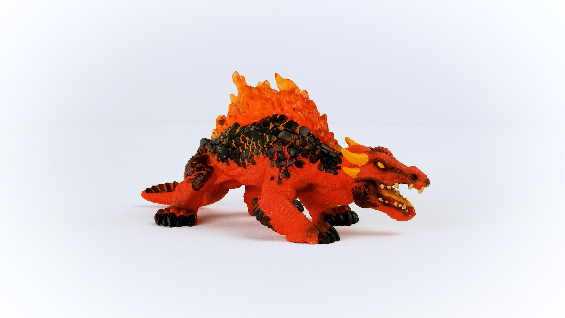 Ein roter und schwarzer Spielzeugdrache mit orangefarbenen Flammen auf dem Rücken, auf weißem Grund.