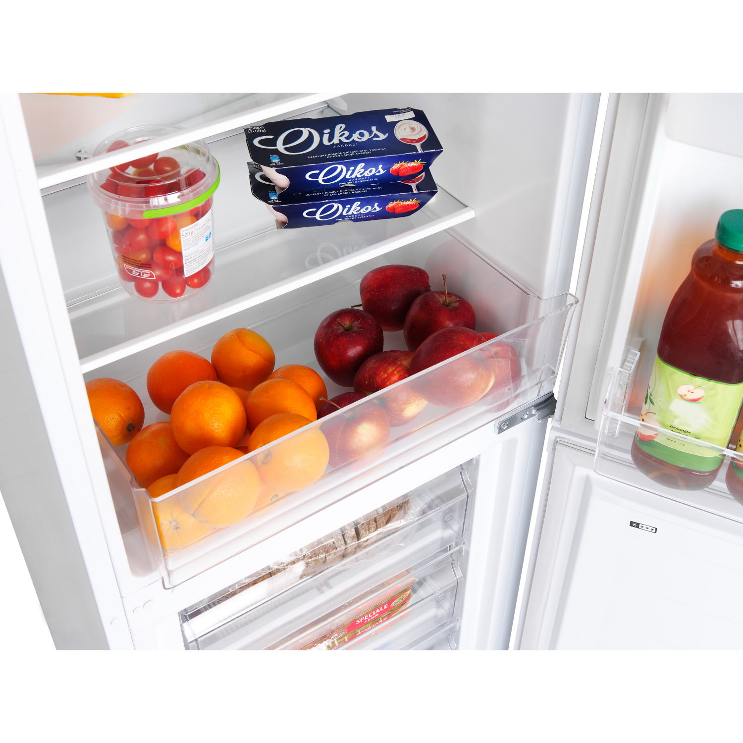 Refrigerator interior with fruits, yogurt, and juice. Oranges, apples, and tomatoes are visible.