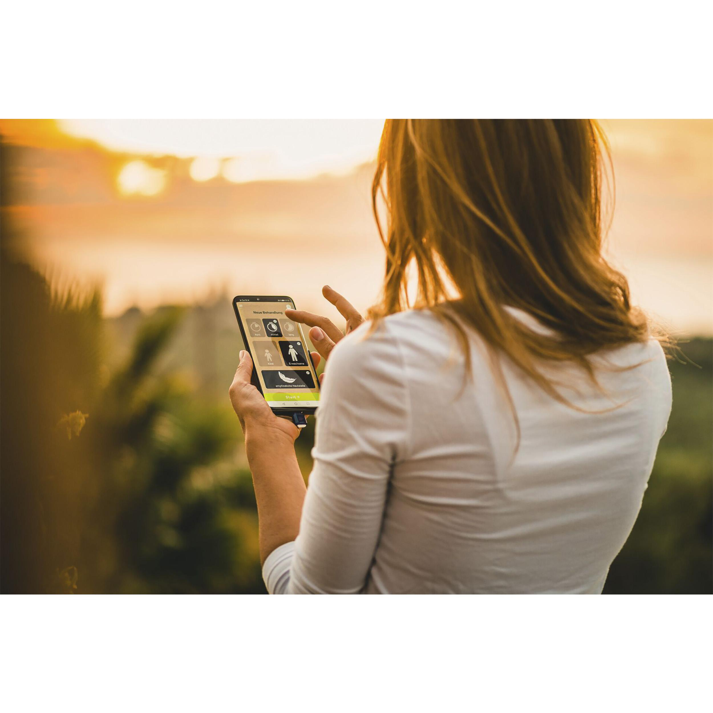 Frau benutzt ein Smartphone im Freien, mit Blick auf eine Landschaft bei Sonnenuntergang.
