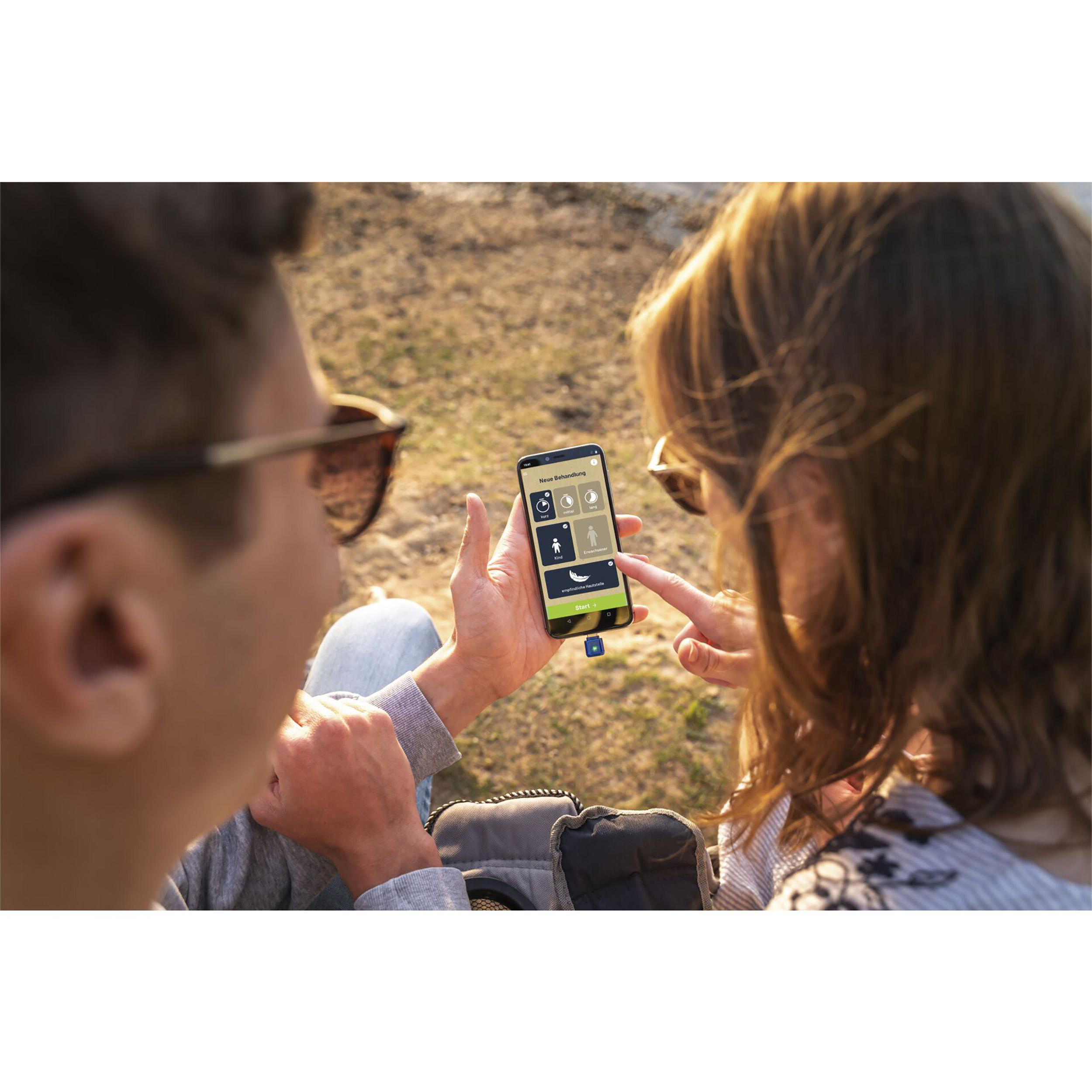 Zwei Personen betrachten einen Telefonbildschirm mit App-Symbolen in einer sonnigen Umgebung im Freien.