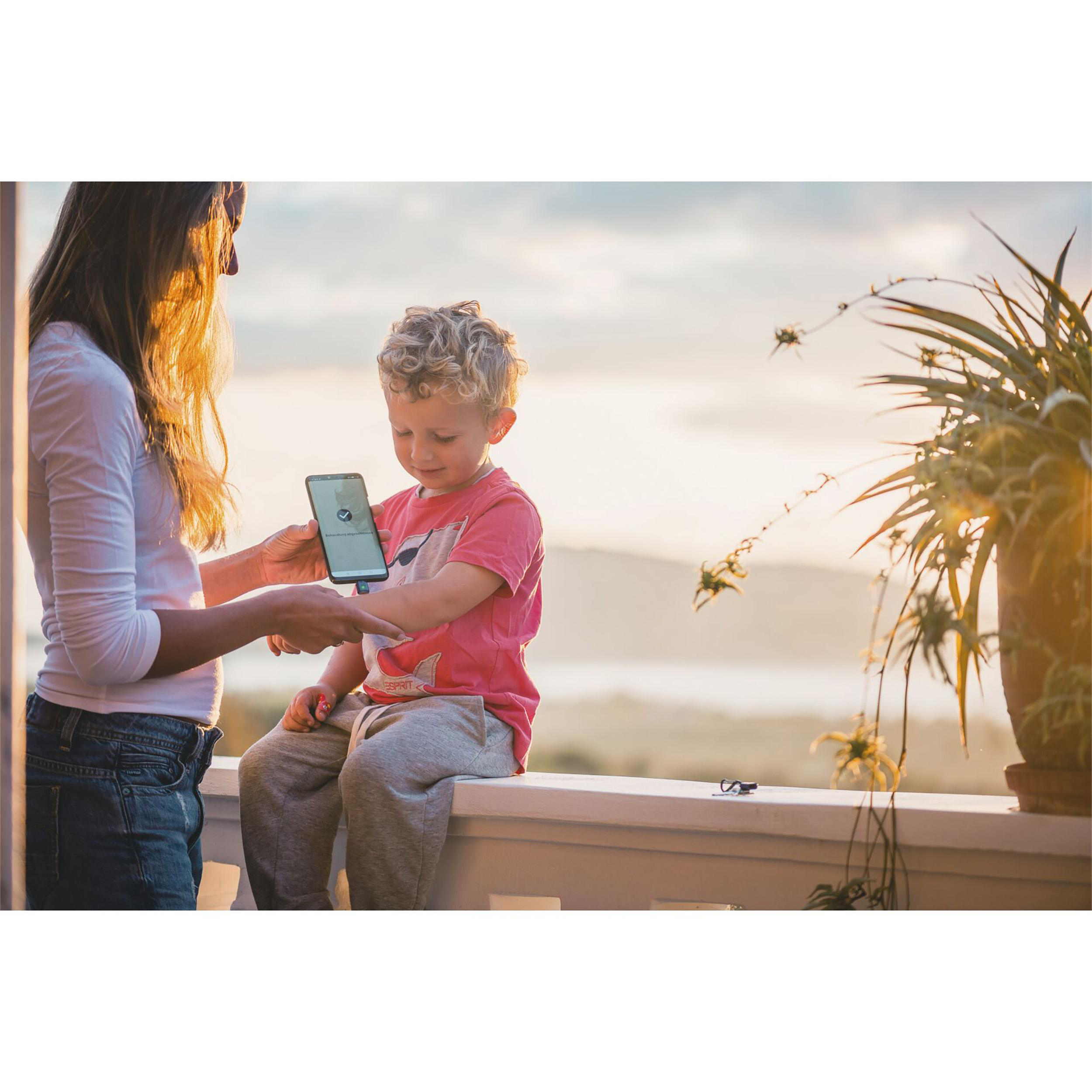 Eine Frau und ein Kind betrachten ein Telefon auf einem Balkon mit Sonnenuntergang im Hintergrund.