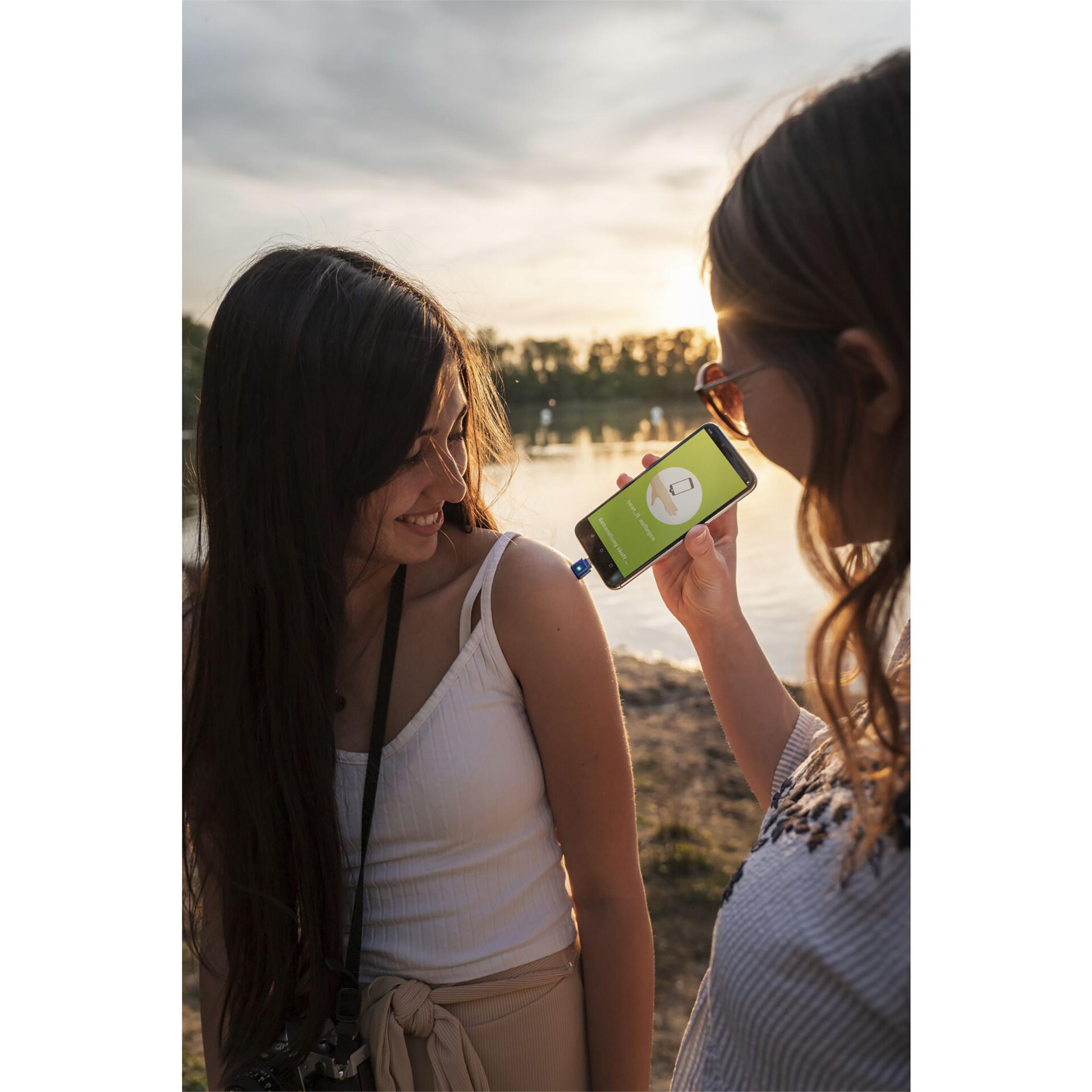 Zwei Frauen am Wasser, eine zeigt ein Telefon mit grünem Bild.