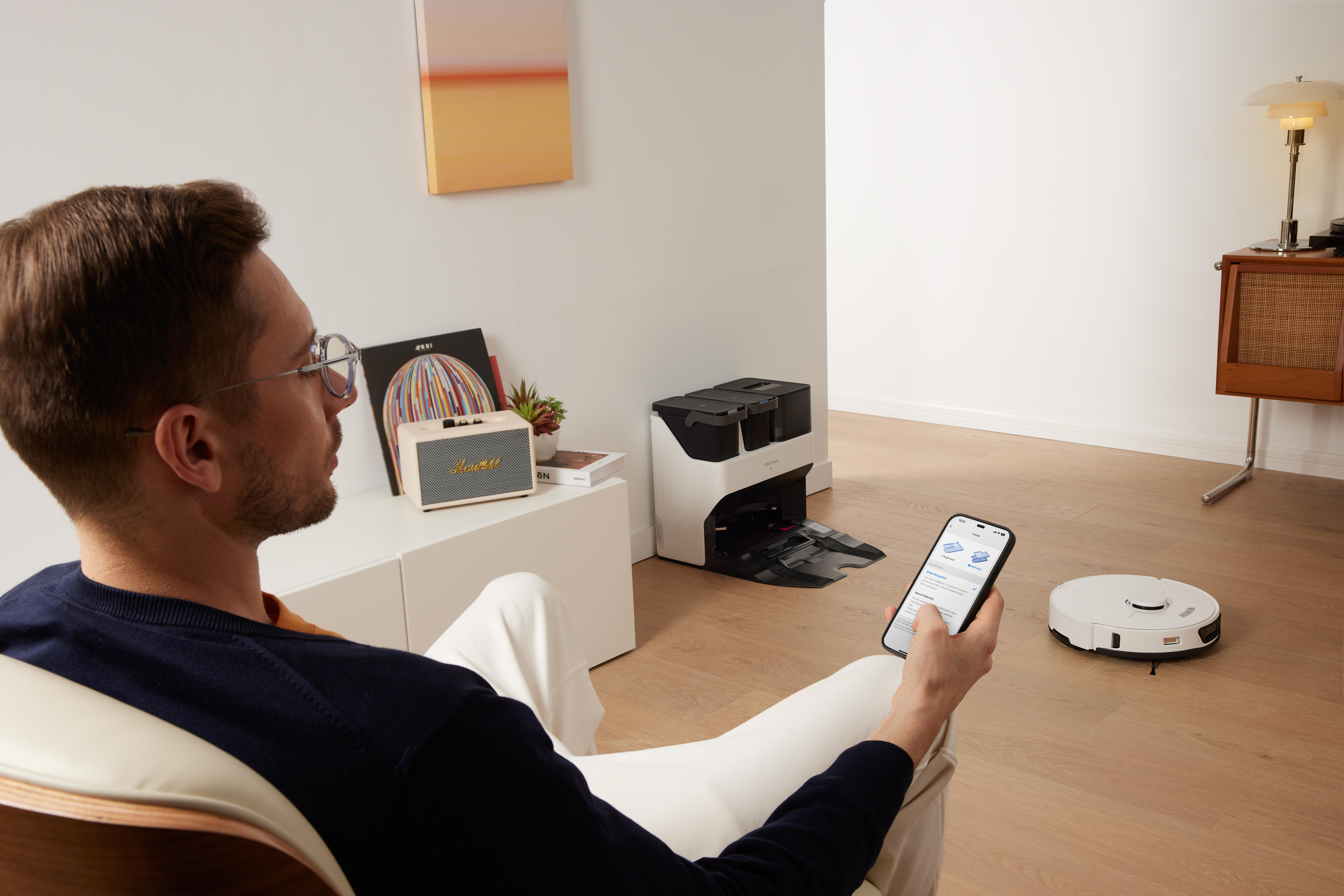 Mann im Wohnzimmer mit Telefon, Roboterstaubsauger auf dem Boden.