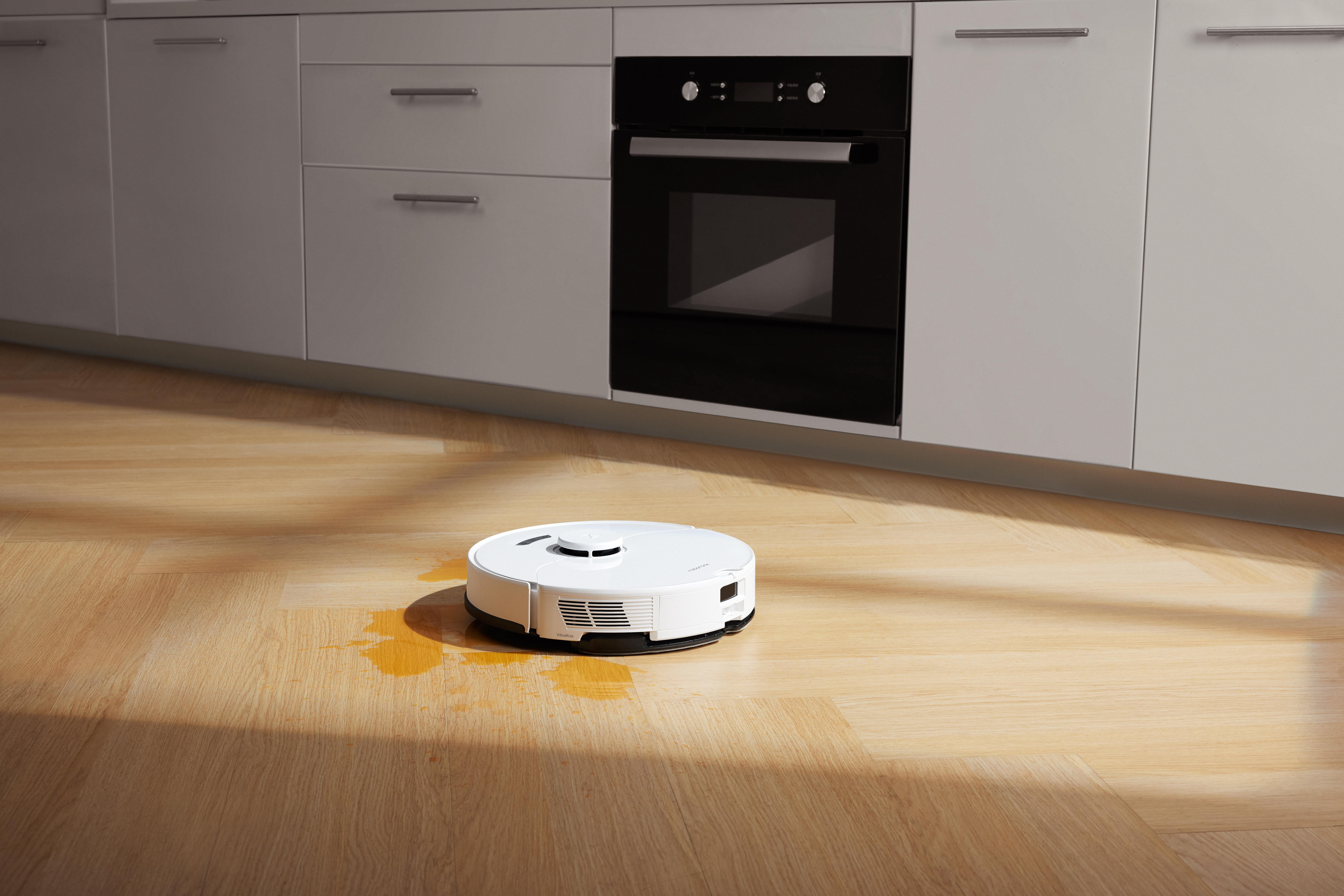 Weißer Roboter-Staubsauger auf Holzboden, mit Wasserspritzer auf dem Boden.