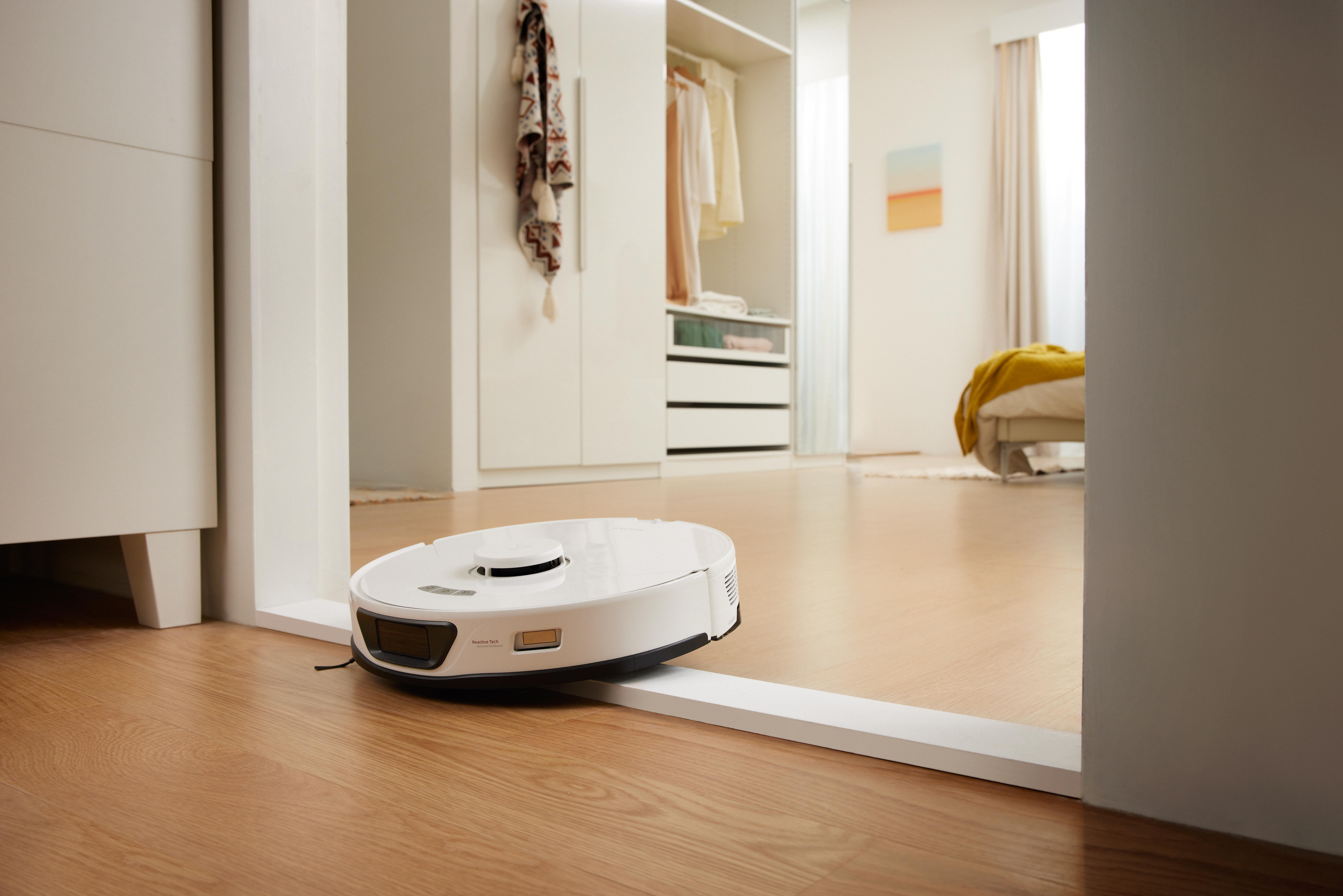 Weißer Roboter-Staubsauger in einem Raum. Holzboden, weiße Möbel und Türrahmen.