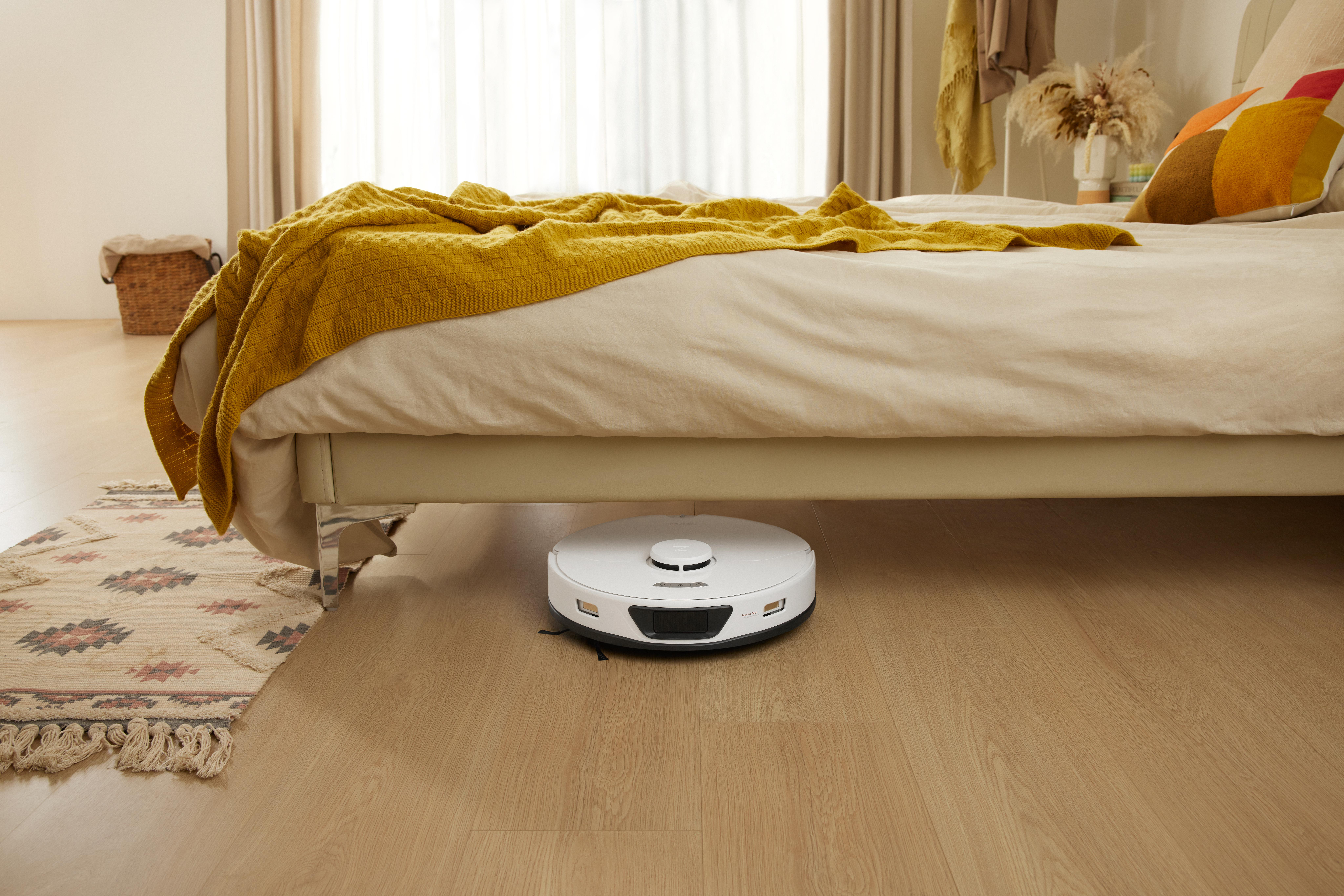 Ein weißer Roboter-Staubsauger unter einem Bett mit gelber Decke.