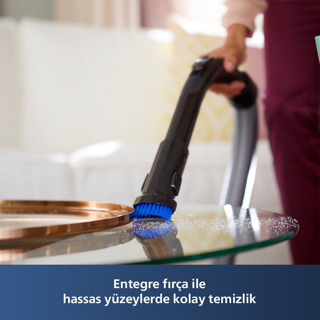 Bir kişi, bir elektrik süpürgesi ve mavi bir fırça ile bir masayı süpürüyor.