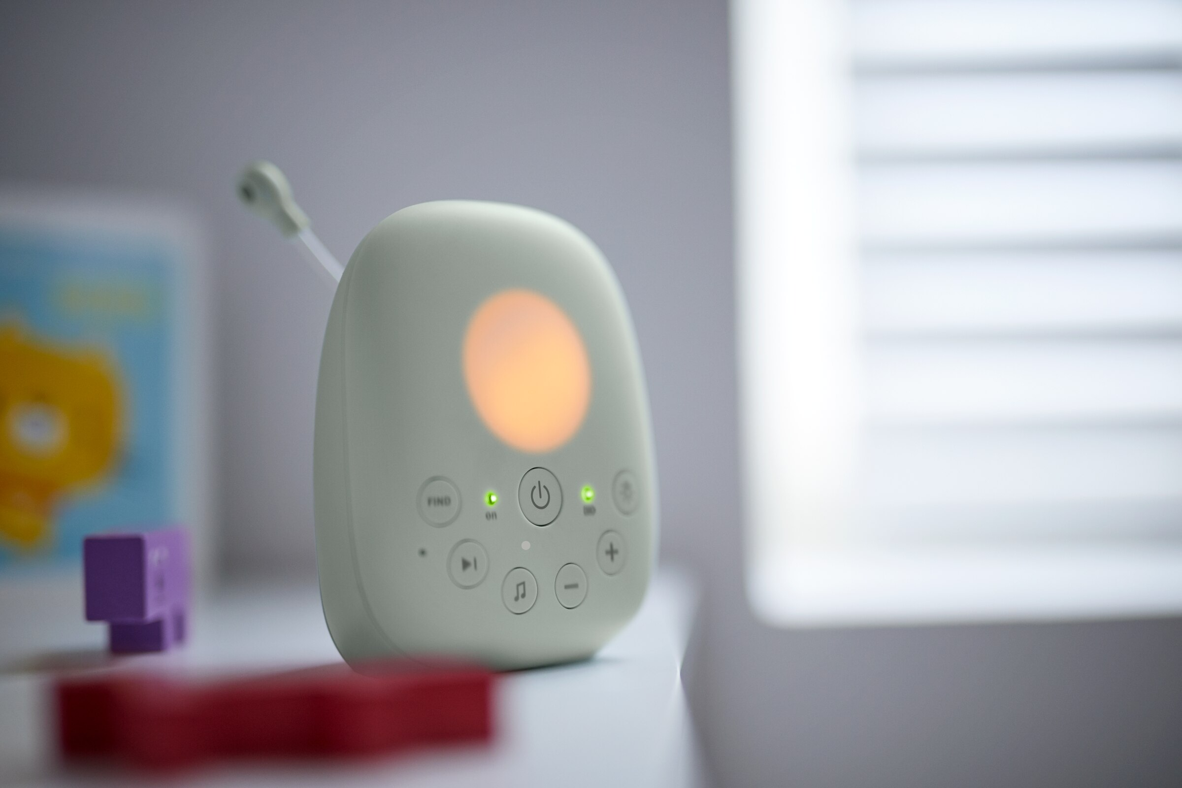 Niania elektroniczna na białej powierzchni, z delikatnym światłem.