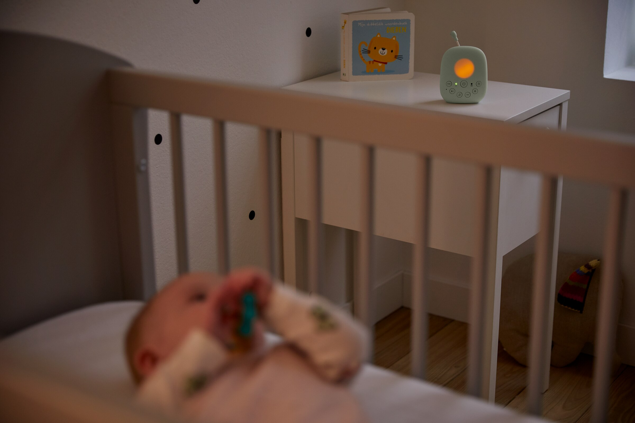 Niania elektroniczna na szafce nocnej. Dziecko w łóżeczku na pierwszym planie.