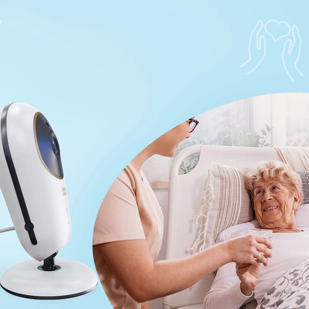 Kobieta podaje wodę starszej pacjentce w łóżku, z kamerą przy łóżku.