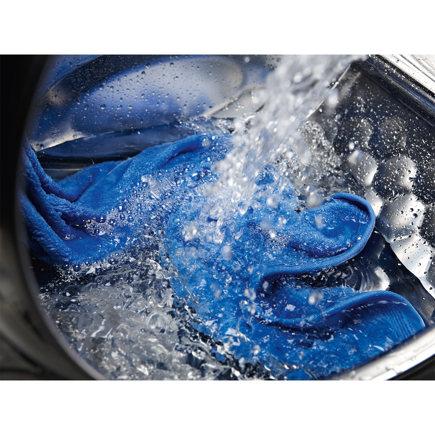 Acqua versata su tessuto blu in un cestello di lavatrice in acciaio inox.