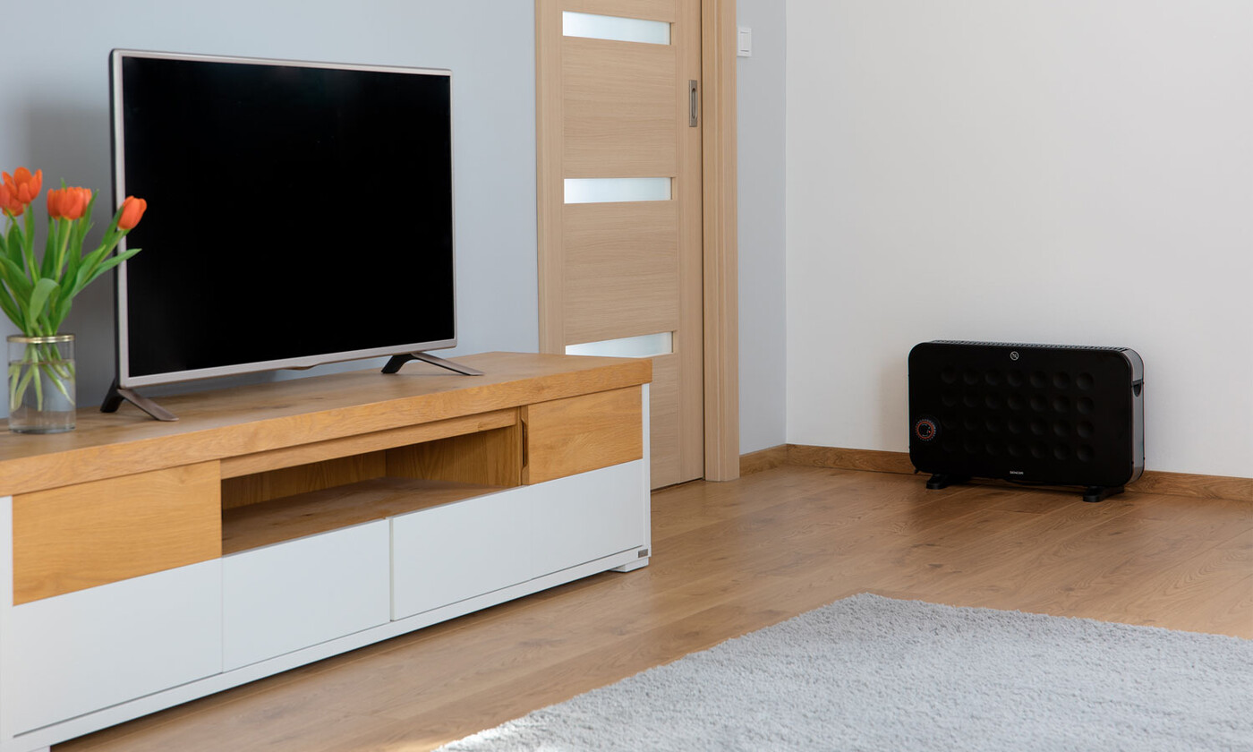 Nappali fa állványon lévő TV-vel, fekete fűtőtesttel és egy ajtóval. Narancssárga tulipánok vannak egy vázában.
