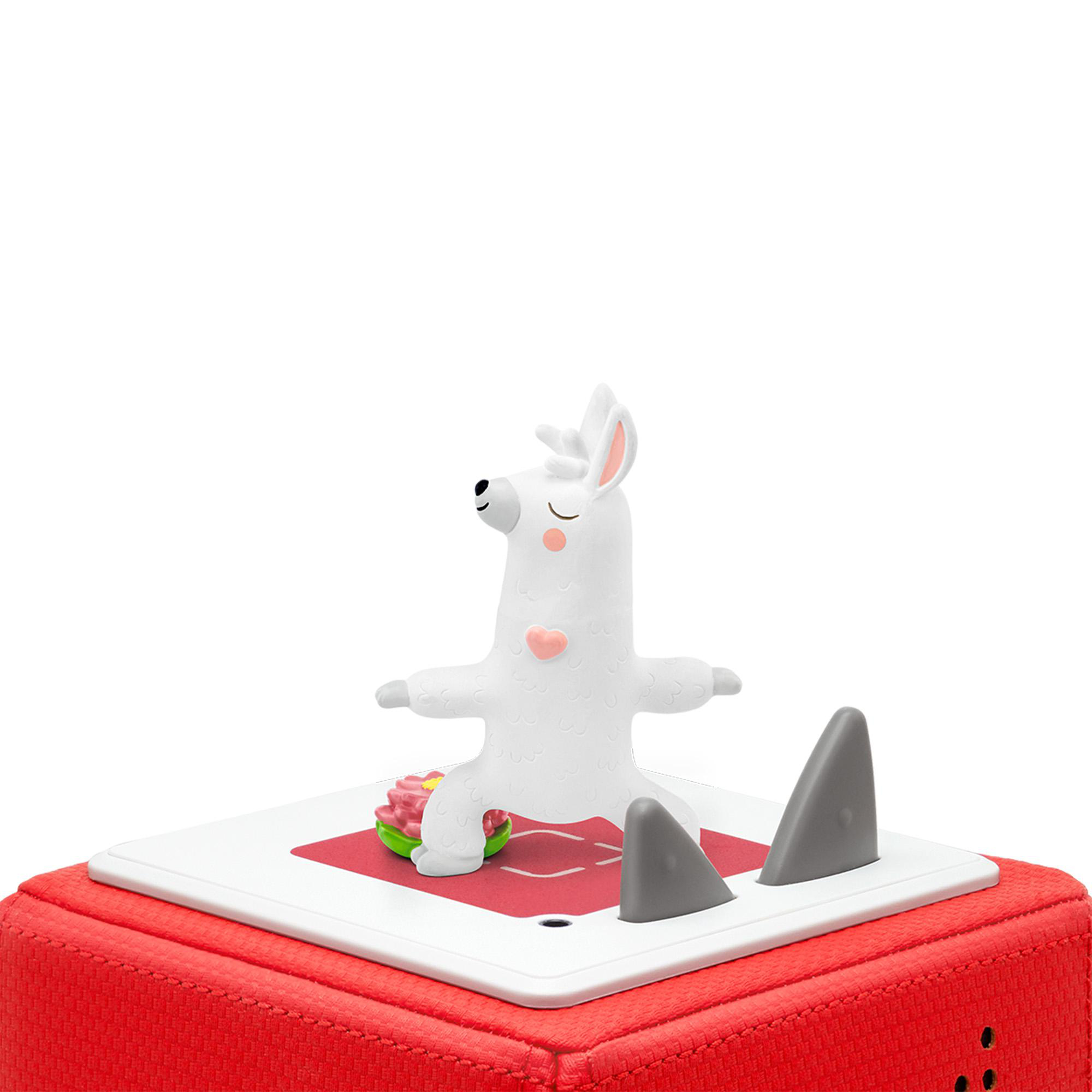 Ein weißes Lama-Spielzeug, das Yoga auf einem roten Würfel mit grauen Haifischflossen macht.