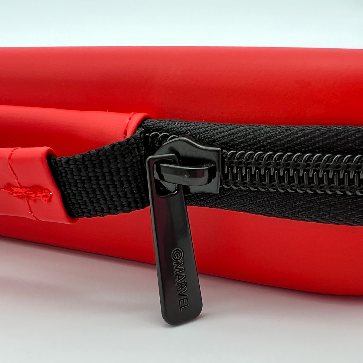 Estuche rojo rectangular con cremallera negra y tirador negro con texto 'MARVEL'.