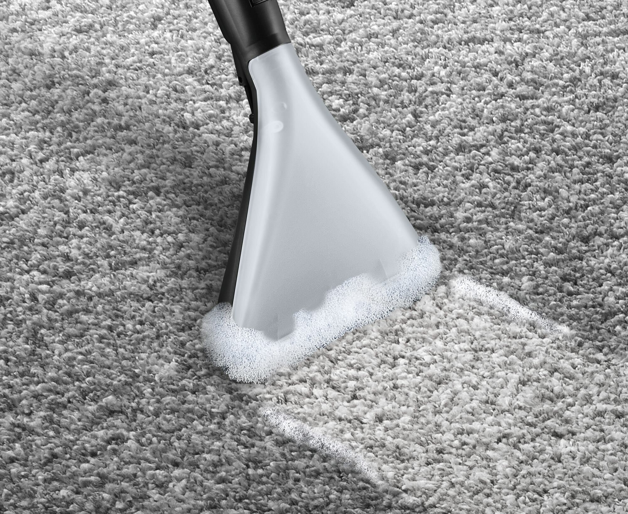 Głowica odkurzacza czyszcząca szary dywan, wytwarzająca białą pianę.