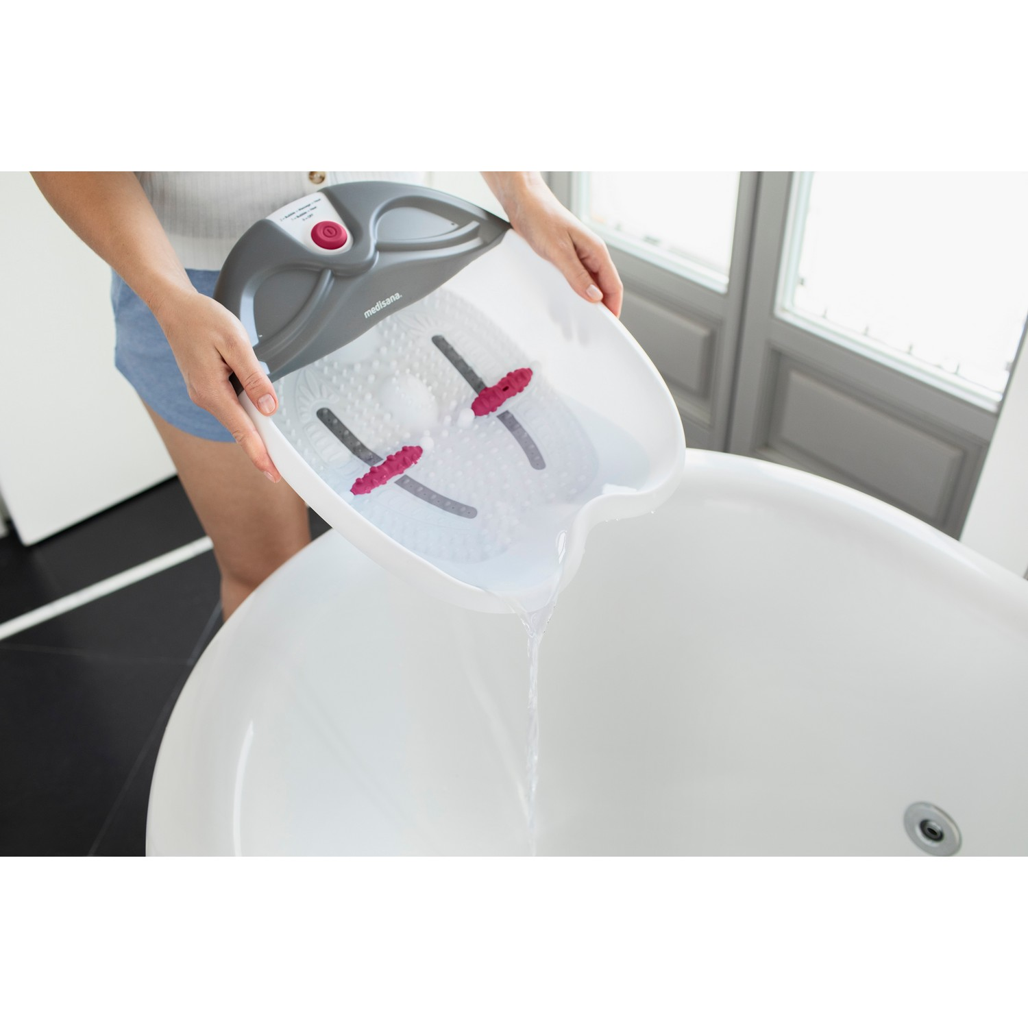 Une personne verse de l'eau d'un bain de pieds dans une baignoire.