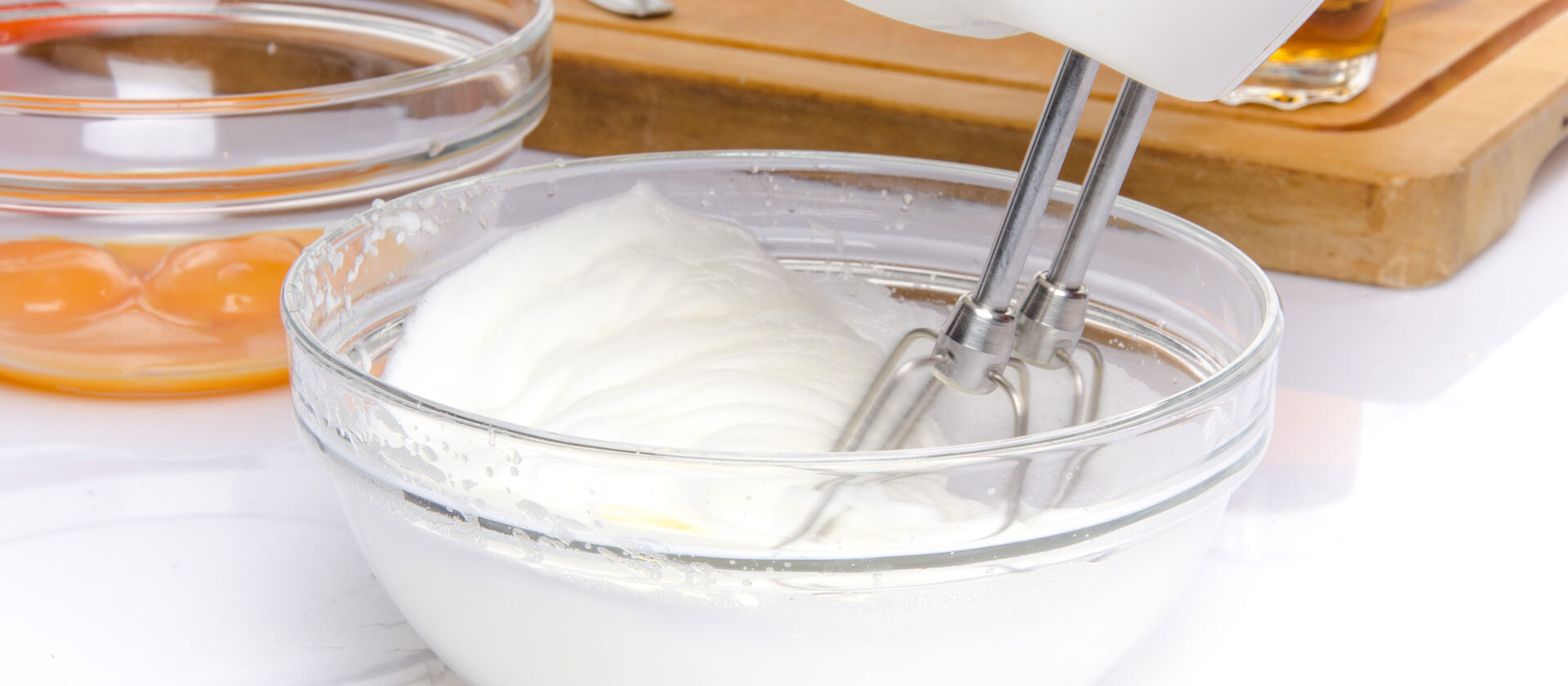 Üvegtál habbal, kézi mixer használatban, tojássárgájával és egy vágódeszkával.