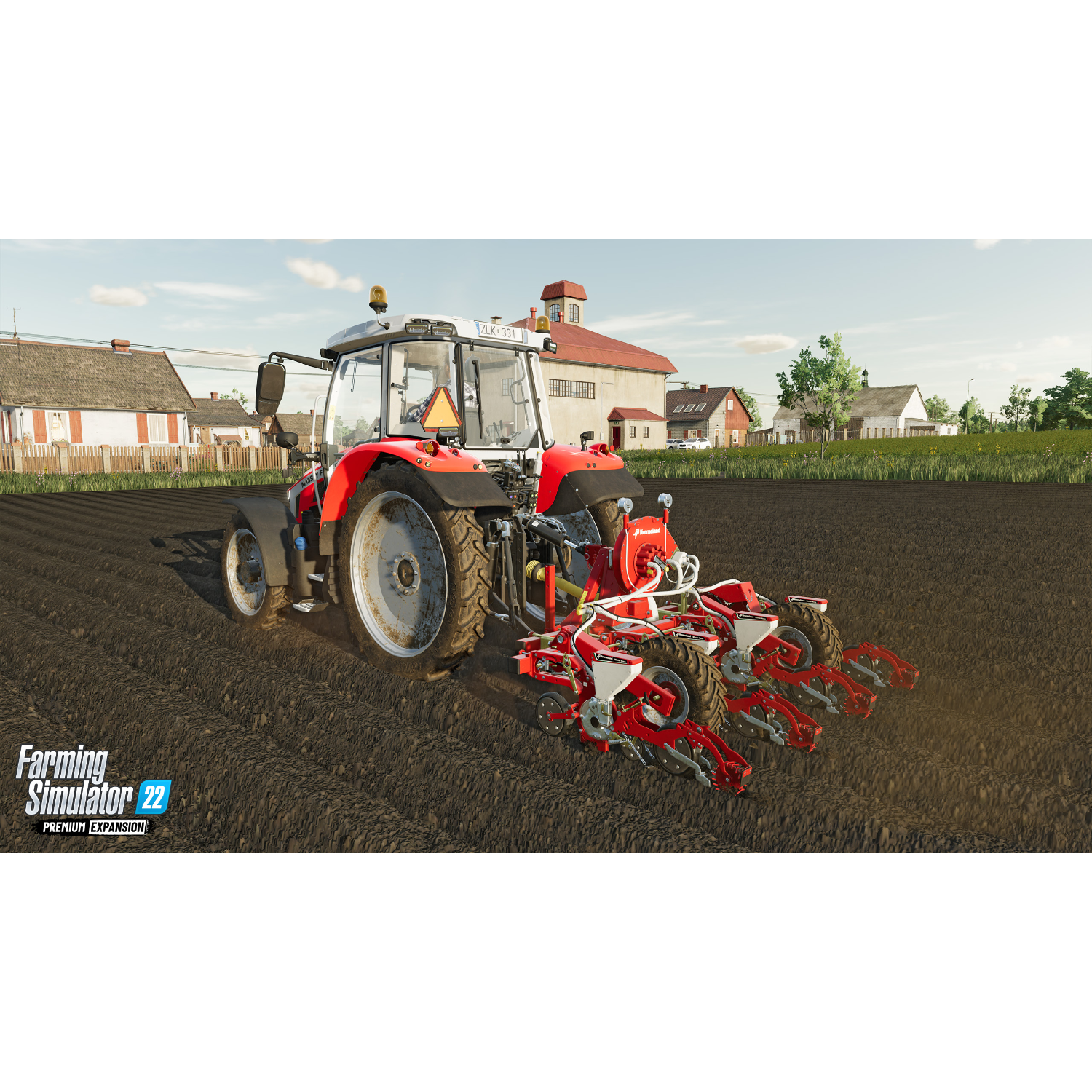 Rode tractor ploegt een veld, met gebouwen op de achtergrond onder een blauwe hemel.