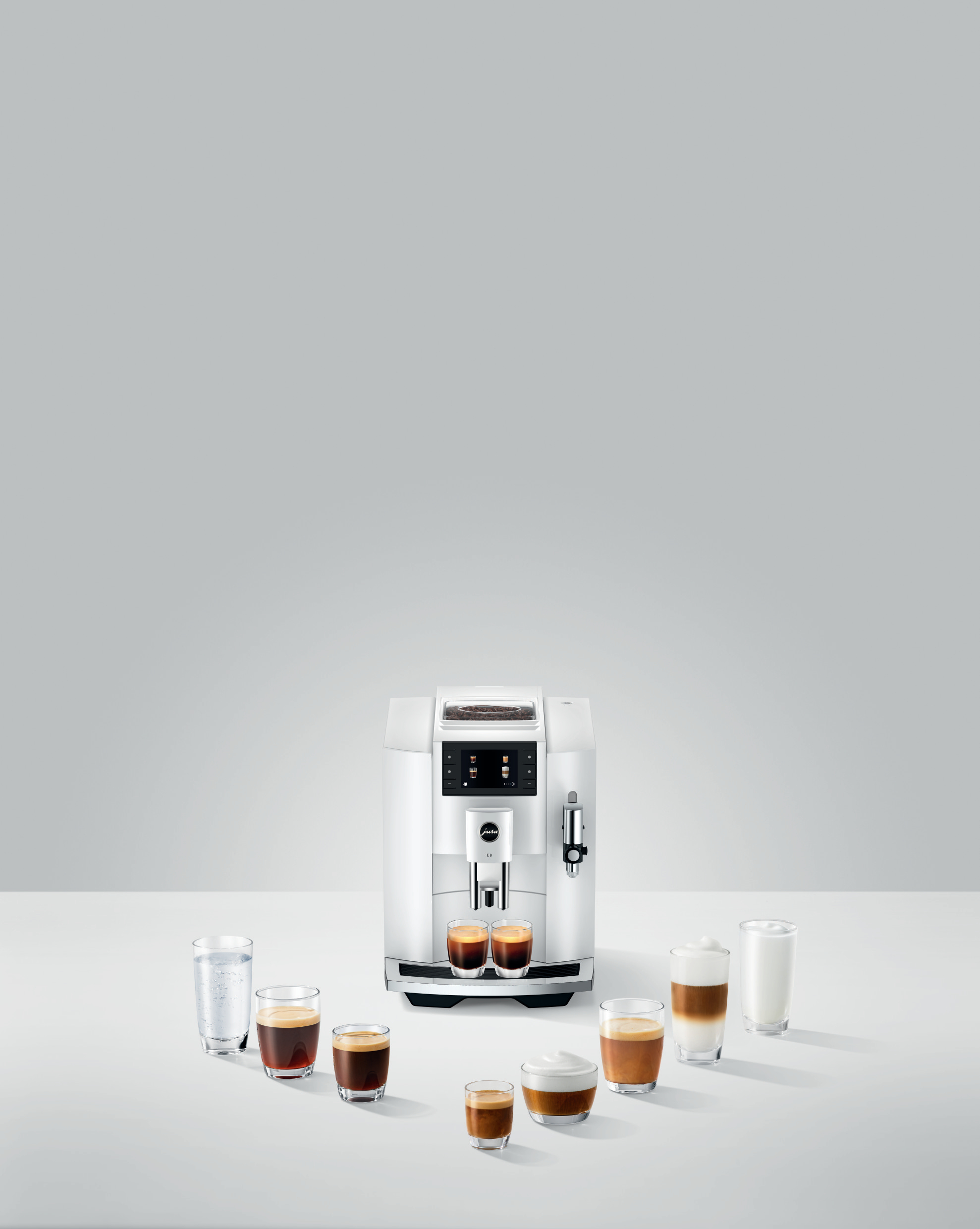 Weiße Kaffeemaschine mit verschiedenen Kaffeegetränken in Gläsern. Grauer Hintergrund.