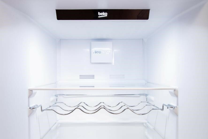 Wnętrze białej lodówki. Jest półka z uchwytami na wino i etykieta NeoFrost.