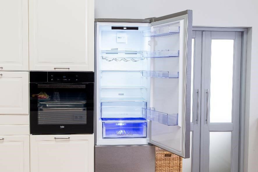 Lodówka do zabudowy z otwartymi drzwiami, pokazująca półki, szuflady i oświetlenie wewnętrzne.