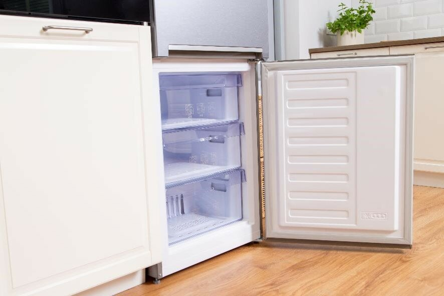 Otwarta lodówka z szufladami zamrażarki. Widoczne białe drzwi i półki wewnętrzne.