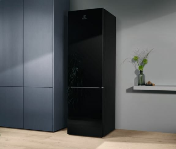 Czarna lodówka Electrolux. Jest umieszczona przy szarej ścianie obok szarej szafki i wazonu.