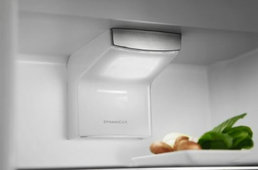 Wnętrze lodówki. Białe wnętrze ze światłem i warzywami na tacy.