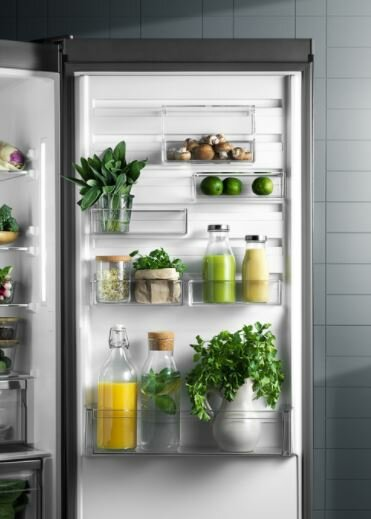 Wnętrze lodówki z półkami i produktami spożywczymi. Widoczne są zielone warzywa i butelki.