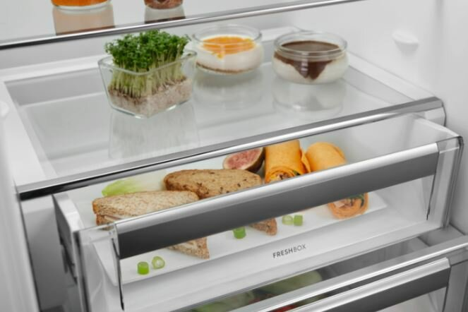 Lodówka pokazuje półki z jedzeniem, w tym świeże zioła i warzywa.