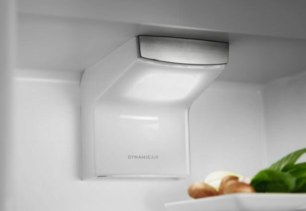 Wewnątrz lodówki, biała oprawa oświetleniowa i talerz z jedzeniem.