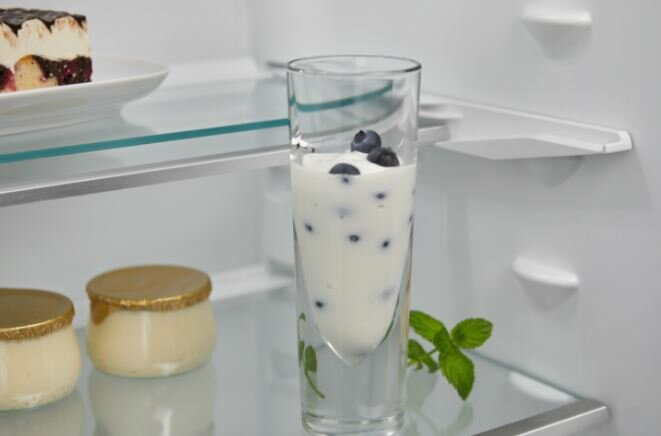 Wysoka szklanka z jogurtem i jagodami. Dwa małe słoiczki i listek mięty.