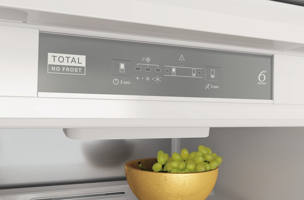 Panel sterowania lodówki z przyciskami i symbolami. Winogrona w złotym naczyniu poniżej.