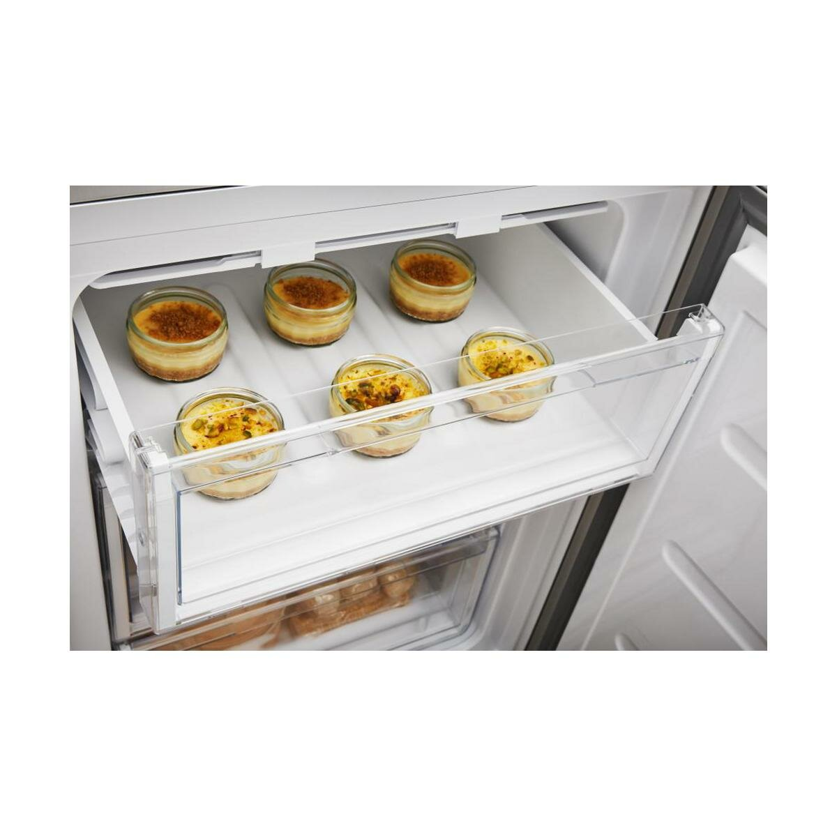 Szuflada lodówki z sześcioma małymi deserami w szklanych pojemnikach, na białej powierzchni.